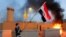 Un manifestante sostiene una bandera iraquí durante una protesta para condenar los ataques aéreos en bases de Hashd al-Shaabi (fuerzas paramilitares), frente a la puerta principal de la embajada de EEUU en Bagdad.